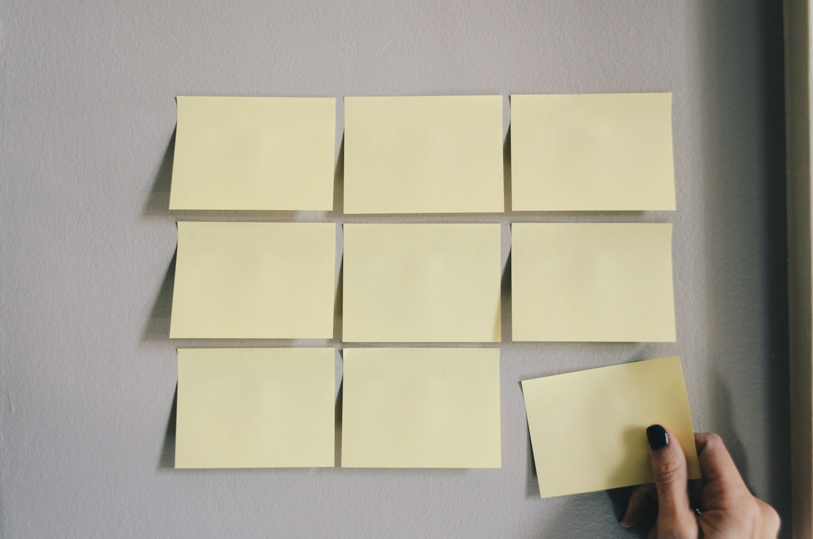 Matriz de notas adhesivas organizadas en filas y columnas sobre pared gris