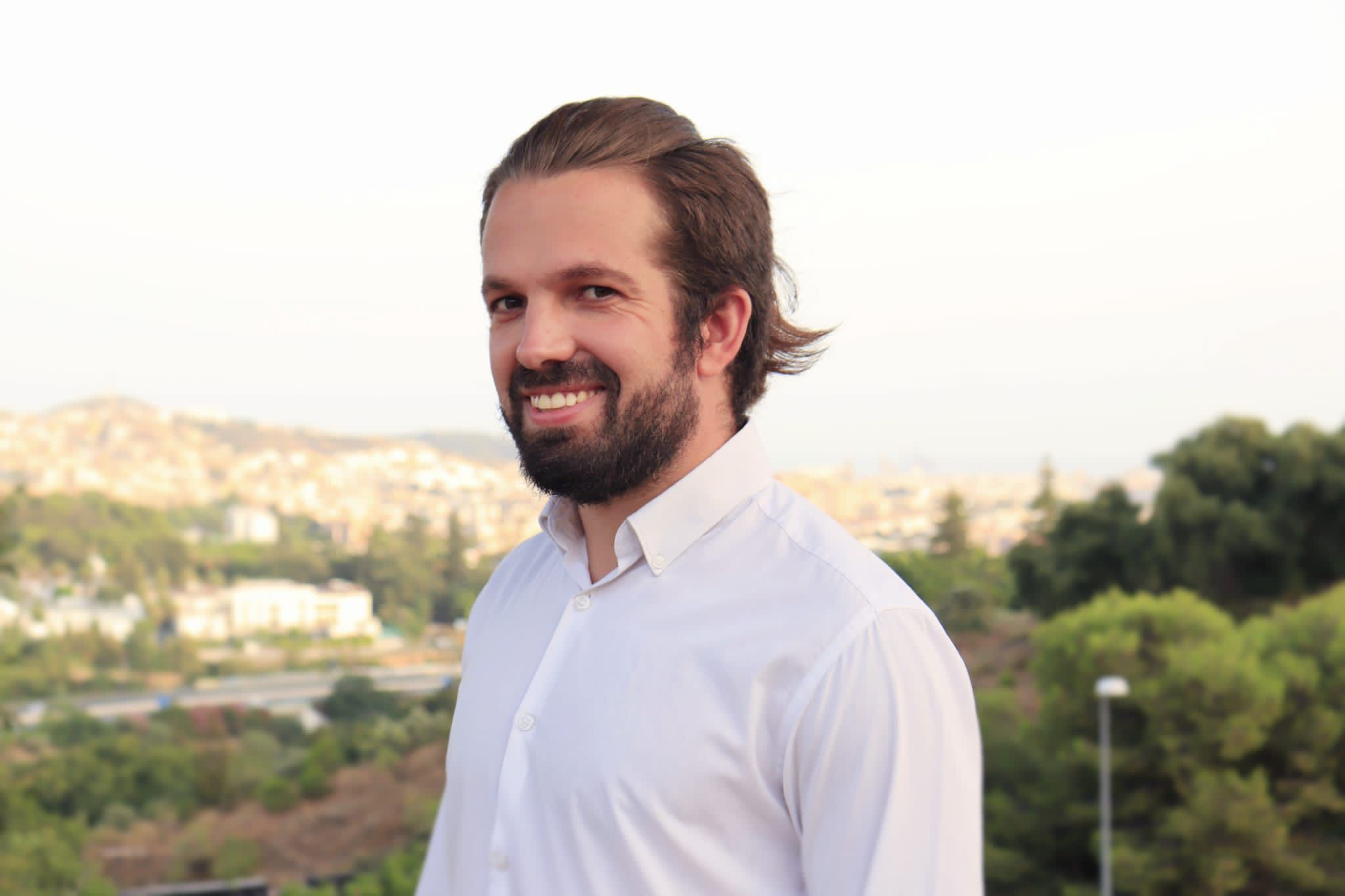 Retrato de Adrián Mariscal con camisa blanca en exterior, con la ciudad al fondo